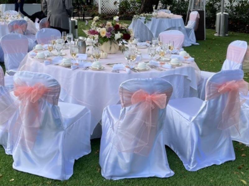 Elegant Outdoor Party Setup With Tablecloths, Overlays, Chairs Covers, Sashes, & Floral Centerpiece